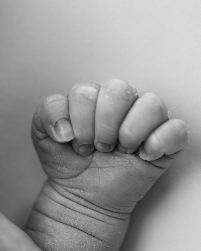 Black-and-white close-up of a newborn baby’s tiny hand gently curled into a fist.
