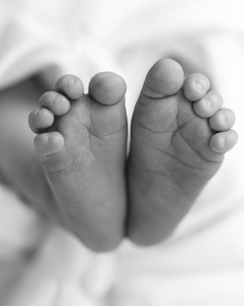 Black-and-white close-up of a newborn baby’s tiny feet, highlighting delicate toes and details.