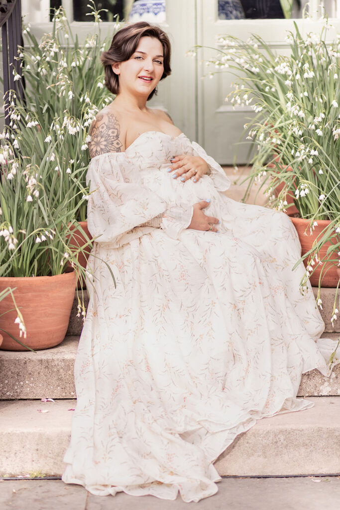 Pregnant woman in flowing white dress seated in the garden during a Bay Area maternity photoshoot