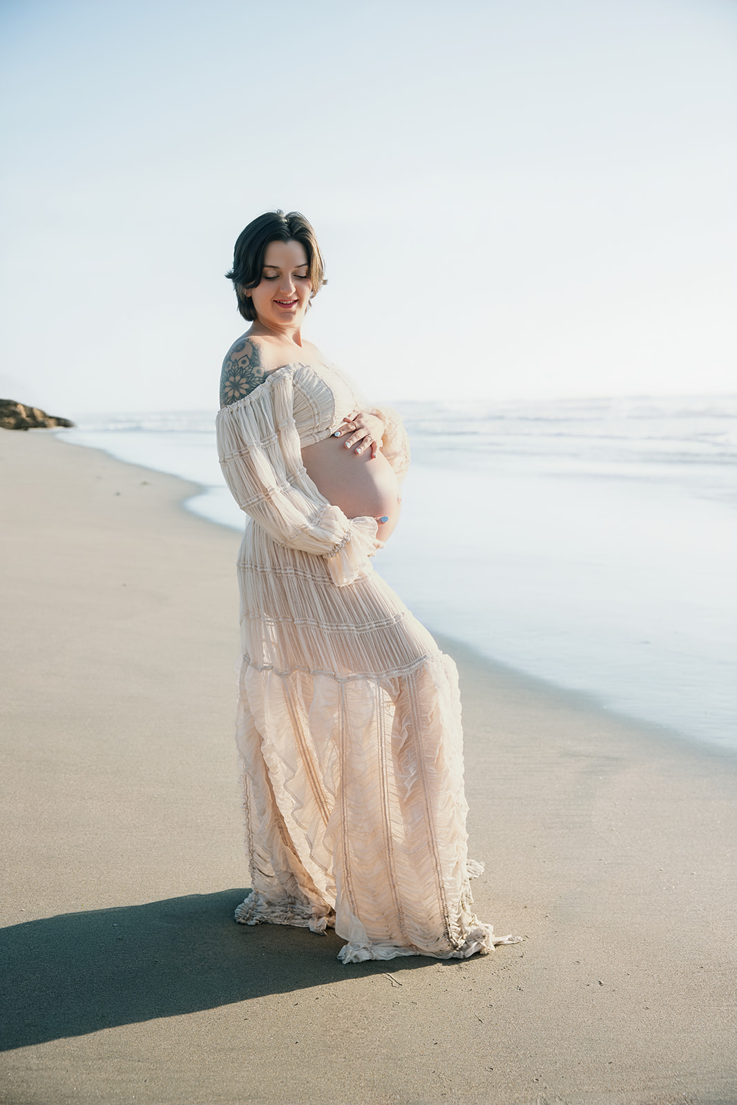 Expecting mother standing on the beach and gently holding her baby bump.
