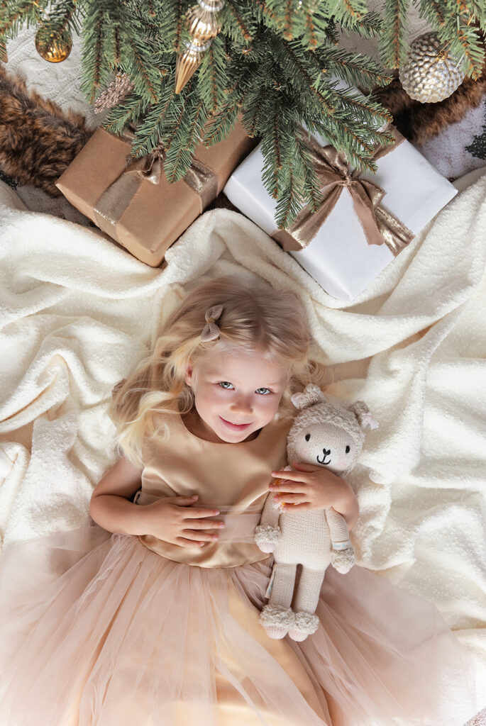 Young girl surrounded by Christmas presents and greenery during a festive holiday photography session