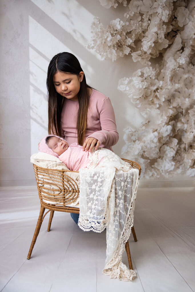Young girl gently sitting beside her sleeping newborn sibling during a cozy sibling newborn photography session.
