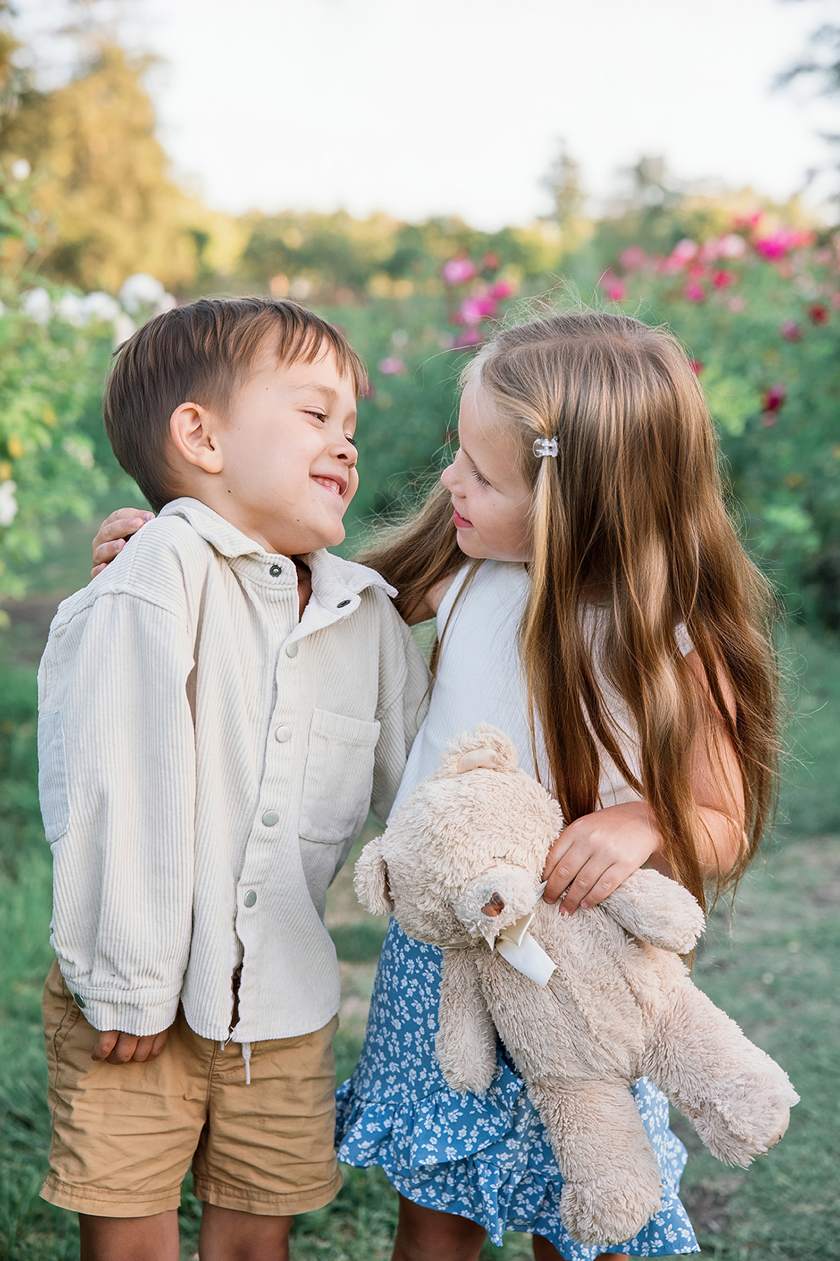 Bay Area family photography: Young brother and sister smiling and sharing a playful moment in a flower garden during golden hour.