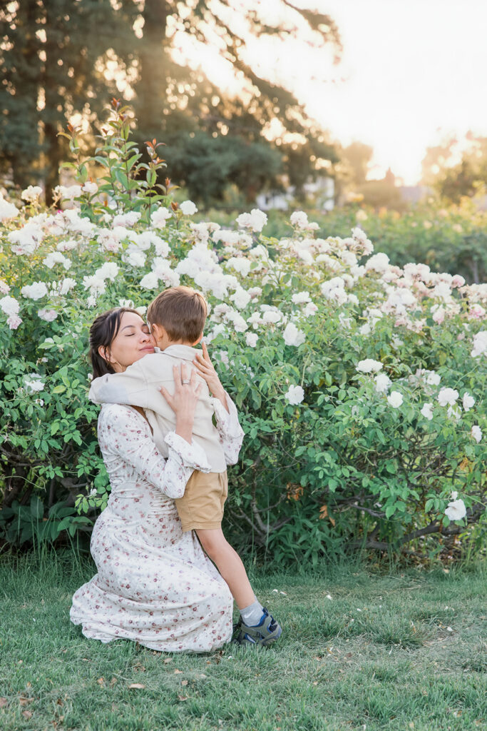 Golden hour family photography: Mother embracing her two children in a blooming garden during a relaxed outdoor family session.