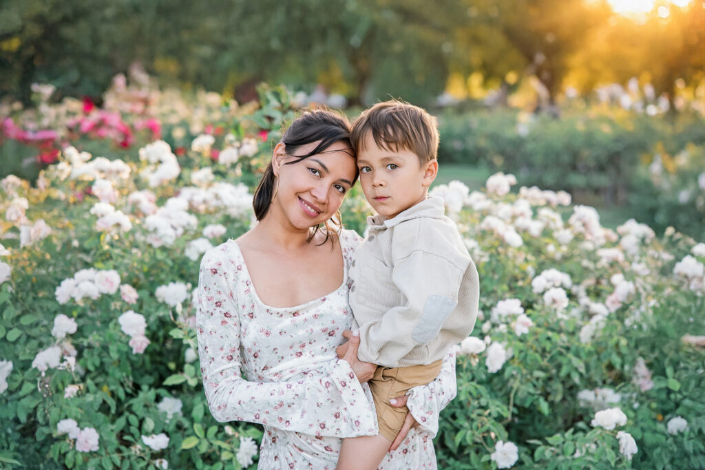 Mother and young son sharing a moment in a flower garden during golden hour, illustrating the best time for outdoor photos.