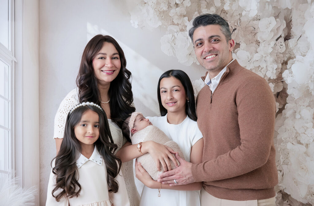 Parents and three daughters smiling together while welcoming their newborn baby during a studio newborn session in San Ramon.