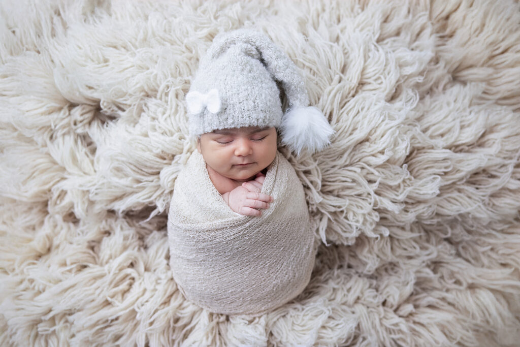 Newborn baby girl peacefully sleeping on a textured cream blanket, photographed in a soft neutral studio setup by FrameIt Bay Area.