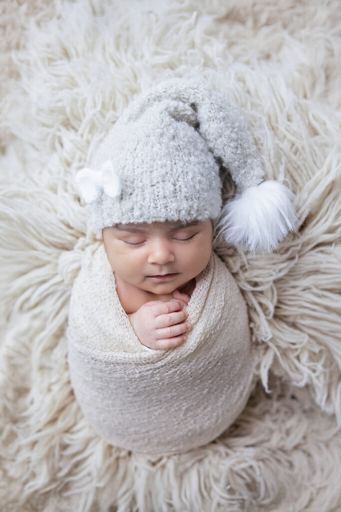 Sleeping newborn baby girl wearing a white knit hat and wrapped in a soft cream blanket during a San Ramon studio newborn photography session.