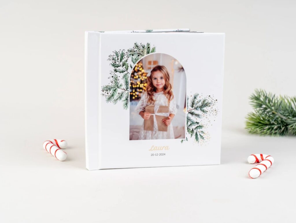 White heirloom photo album featuring a little girl holding a wrapped Christmas gift, with delicate greenery and festive Christmas details on the cover.