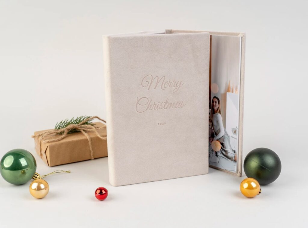 Luxury velvet triplex photo album displayed open to a family portrait, surrounded by festive Christmas ornaments and a wrapped gift.