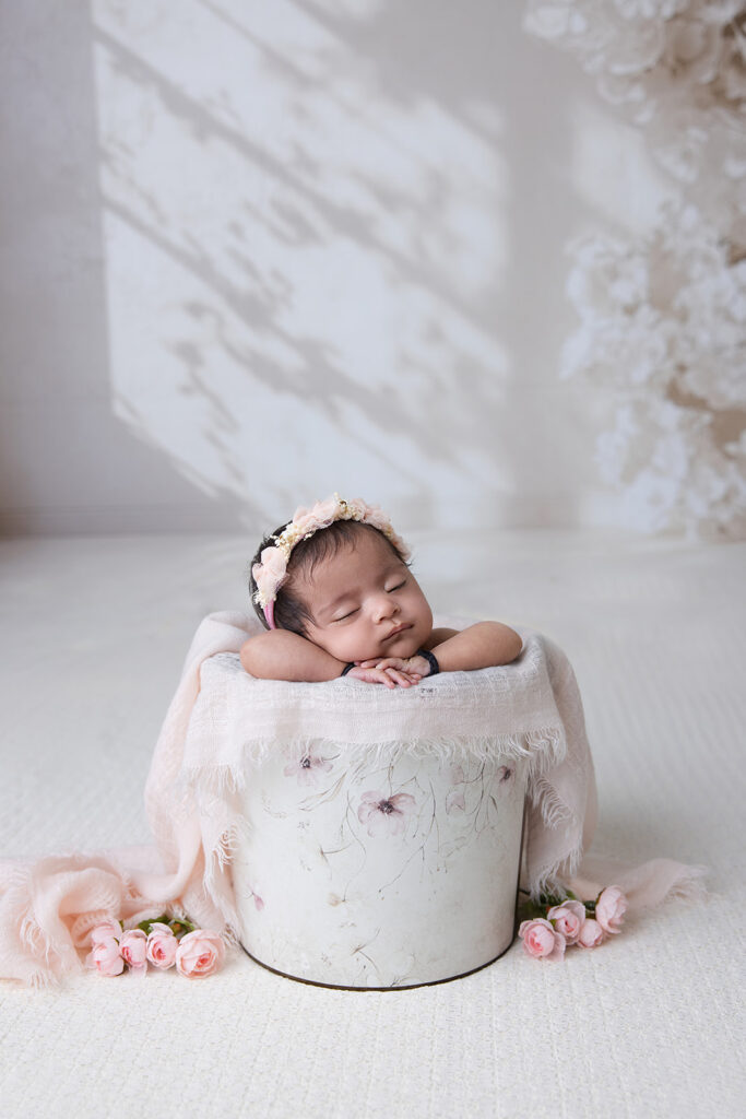 Sleeping newborn baby wrapped in a soft white blanket in a beautifully styled newborn photography setup by FrameIt Bay Area.