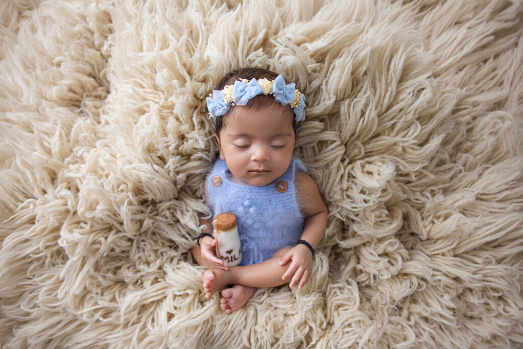 Sleeping newborn baby wearing a blue outfit, photographed from above on a fluffy beige blanket by a San Ramon newborn photographer.