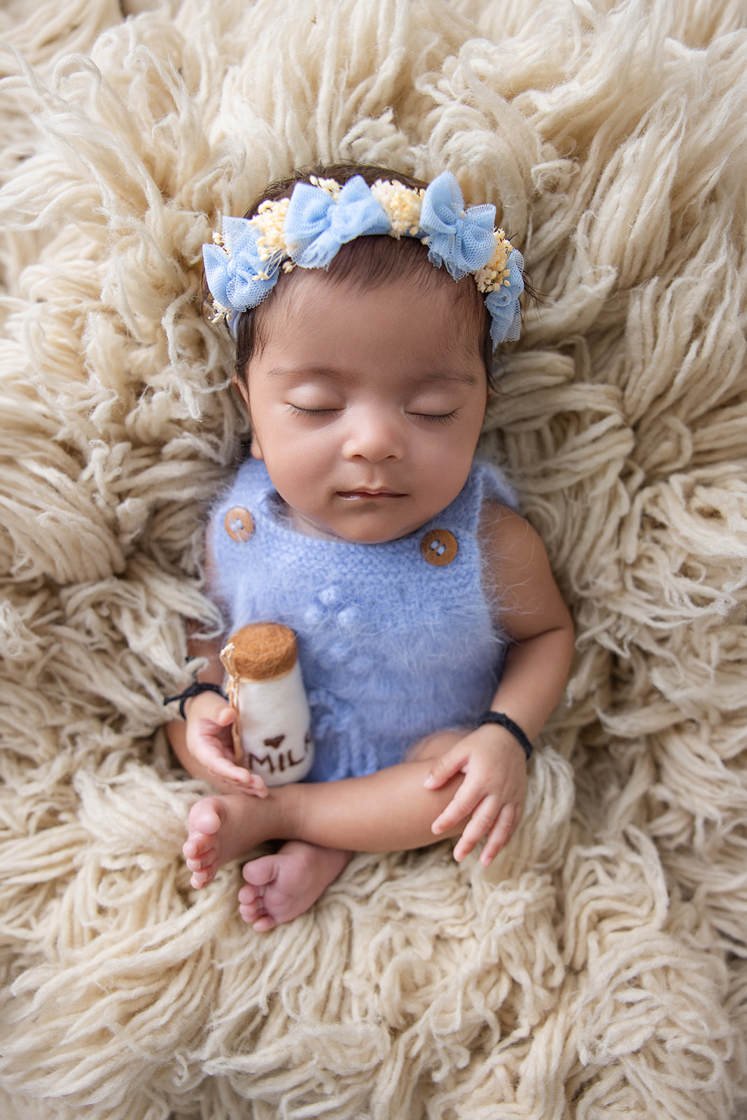 Newborn baby wearing a blue outfit and floral headband, holding a teddy bear during a FrameIt Bay Area newborn photography session.