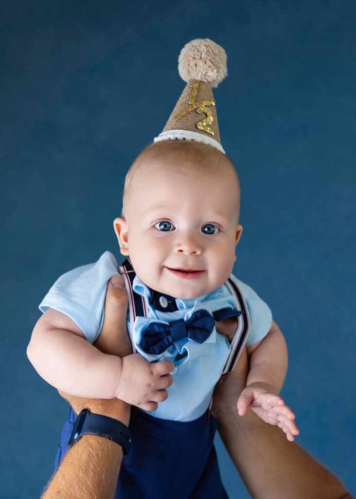 Close-up portrait of a smiling six-month-old baby wearing a birthday hat during a six-month photo session