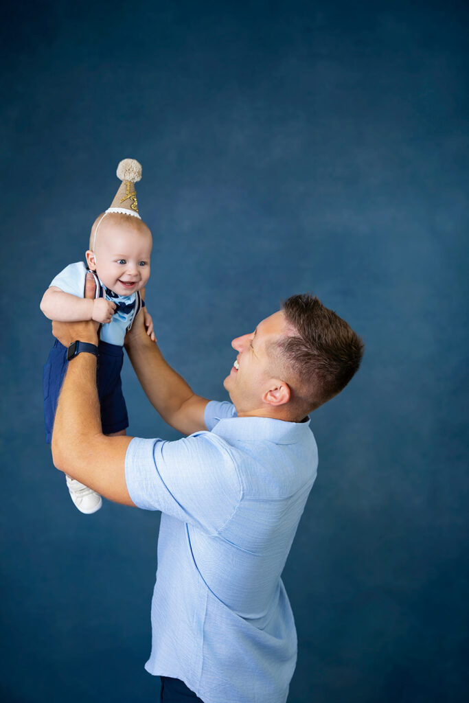 Father lifting his six-month-old baby in the air during a playful milestone photo session