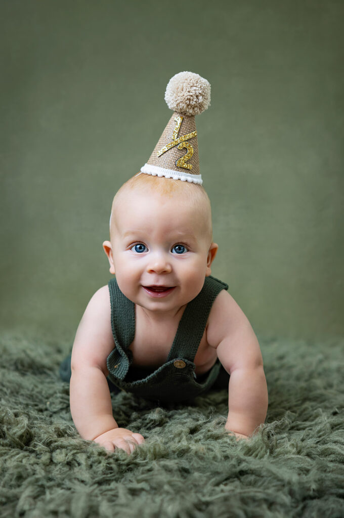 Six-month-old baby smiling while wearing a birthday hat during a six-month milestone photo session