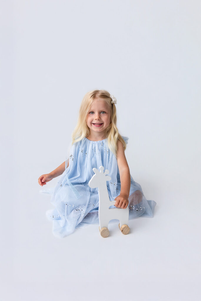 Smiling young girl in a light blue dress during a children’s studio photography session.