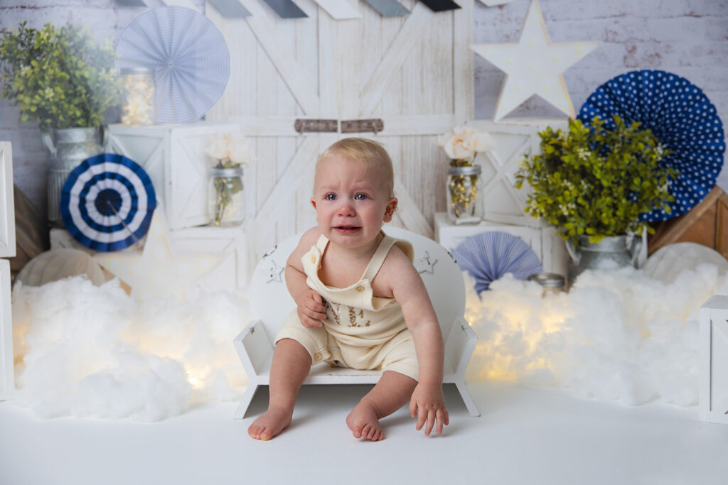 One-year-old baby boy sitting on a white blanket in a first birthday photo setup, showing why family photoshoot tips include allowing children time to warm up.